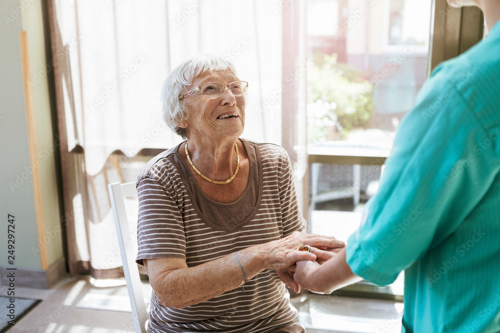 Smiling senior woman holding hands of nurse at home