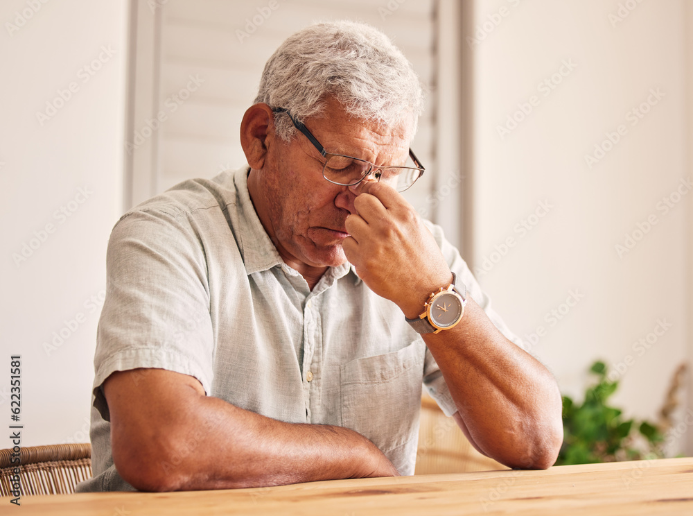 Stress, headache and old man at table in home with glasses, worry and fatigue in retirement. Debt, anxiety and tired, frustrated senior person with mental health problem or crisis, exhausted and sad.
